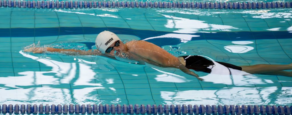 An athlete swims freestyle stroke with focus, showcasing competitive technique in an indoor pool.